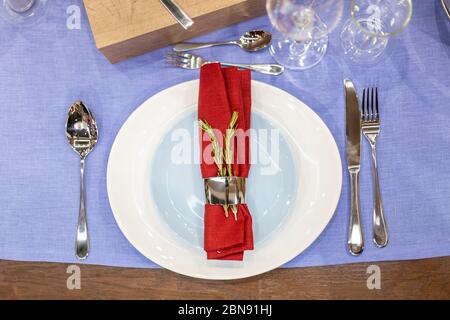 table setting with a blue tablecloth, a white and blue plate, a red napkin in a steel holder, steel appliances, glass goblets. top view, close up Stock Photo