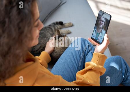 Young hispanic girl sit on sofa with cat hold phone video call on mobile screen. Stock Photo