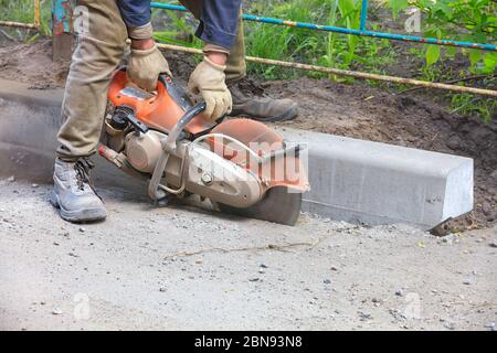 A worker using a concrete cutter cuts asphalt and concrete curbs in a cloud of concrete dust to create a track. Stock Photo