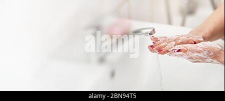 Young woman washing her hands under water tap faucet with soap. Wide banner space for text left side. Personal hygiene concept - coronavirus covid-19 Stock Photo