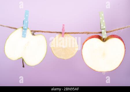 Slices of fruit and vegetables (lemon, cucumber, zucchini) wet on rope with clothespins. Creative idea, imagination and fantasy. Minimal style, purple Stock Photo
