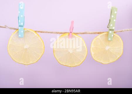 Slices of fruit and vegetables (lemon, cucumber, zucchini) wet on rope with clothespins. Creative idea, imagination and fantasy. Minimal style, purple Stock Photo