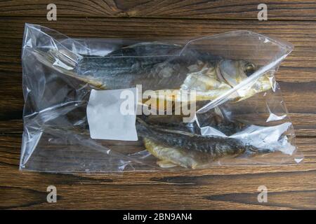 Dried salted crucian fishes in a transparent package with a white label on wooden background. Snack to beer Stock Photo