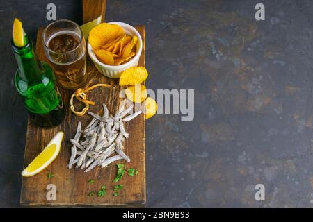 Dried salted anchovies with beer, lemon and potato chips on dark wooden board. Snack on fish with beer. Top views with clear space Stock Photo