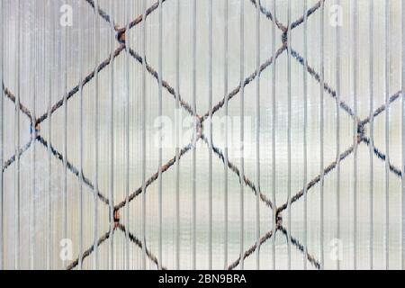 Cells of an iron mesh that shines through the cellular surface of a plastic sheet, to be used as a texture for the background. Stock Photo