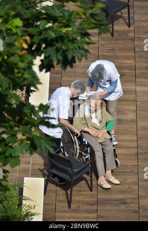 Nurses caring for an elderly and disabled woman in a nursing home on a sunny day during the coronavirus pandemic Covid-19. Carers wear a face mask. Stock Photo