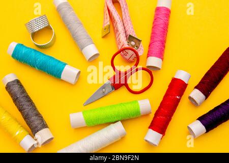 Thread, needles, scissors and meter on yellow background. tailoring set. sewing kit multi-colored Stock Photo