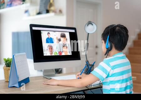 Asian boy student video conference e-learning with teacher and classmates on computer in living room at home. Homeschooling and distance learning ,onl Stock Photo