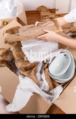 Detail of woman packaging fragile items using crumpled packing paper. Concept of moving in or out. Stock Photo
