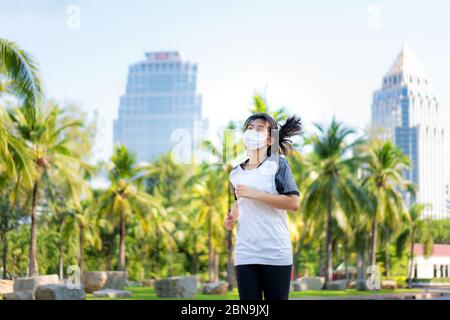 Asian young woman are jogging and exciseing outdoor in city park and wearing protective mask on face for stay in fit during Covid-19 pandemic in Bangk Stock Photo