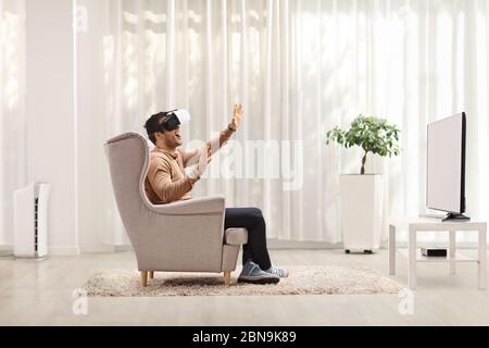 Guy sitting in an armchair and using a VR headset at home Stock Photo