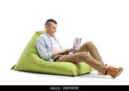 Young man working on a laptop and sitting on a green bean bag isolated on white background Stock Photo