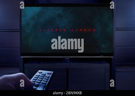 A man points a TV remote at the television which displays the Altered Carbon main title screen (Editorial use only). Stock Photo