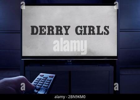 A man points a TV remote at the television which displays the Derry Girls main title screen (Editorial use only). Stock Photo