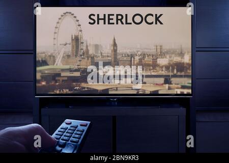 A man points a TV remote at the television which displays the Sherlock main title screen (Editorial use only). Stock Photo