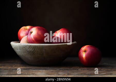 Nectarines in wooden bowl on dark wooden table. Stock Photo