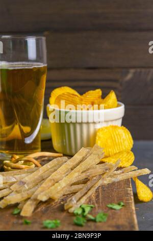 Dried salted tuna elite snack with beer, lemon and potato chips on dark wooden board. Snack on fish with beer. Front views, close-up Stock Photo