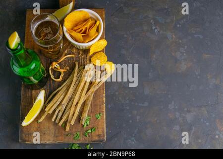 Dried salted tuna elite snack with beer, lemon and potato chips on dark wooden board. Snack on fish with beer. Top views with clear space Stock Photo