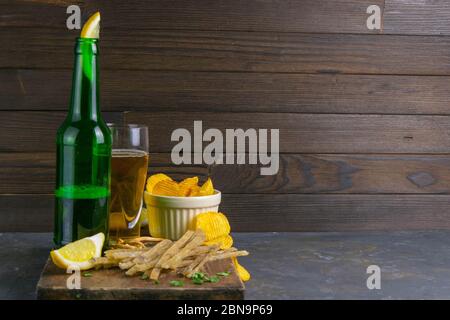 Dried salted tuna meat strips with beer, lemon and potato chips on dark wooden board. Snack on fish with beer. Front views with clear space Stock Photo
