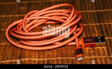 a closeup view of a modern technology red color usb cable stays on the brown bamboo platform, retro-styled. Stock Photo