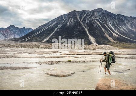 Hiker faces adversity, crossing a braided river channel. Stock Photo