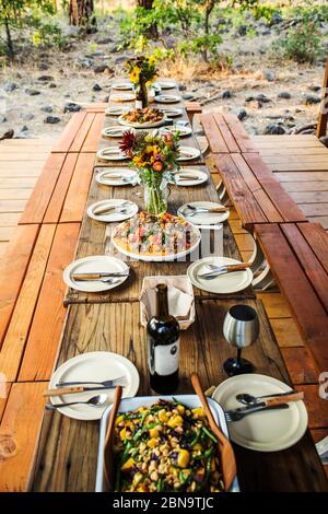 A long wooden table set for dinner in open-air setting Stock Photo