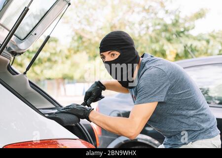 Robber stealing stuff from the car while looking around Stock Photo
