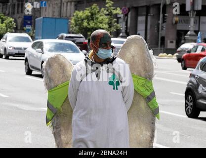 Kiev, Ukraine. 13th May, 2020. A man wearing face mask as a preventive measure against coronavirus and with decorative wings behind his back walks on a street in Kiev, Ukraine, on 13 May 2020. Ukraine began to ease anti-virus restrictions after to months of the quarantine, introduced in the country since 12 March 2020 and extended later until 22 May. Credit: Serg Glovny/ZUMA Wire/Alamy Live News Stock Photo