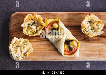 healthy plant-based food recipes concept, filo pastry cups and puff pastry envelopes with vegan cheese pesto and tomato filling on cutting board Stock Photo