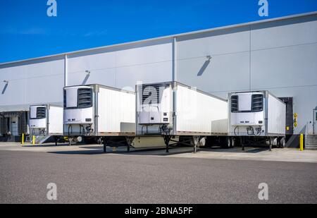 Industrial grade refrigerator semi trailers with reefer units on the front wall and without semi trucks standing at warehouse dock gates loading chill Stock Photo