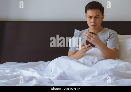 Asian man watching serious online news at smart phone in morning on the bed. Stay home self isolation and quarantine during coronavirus covid-19 pande Stock Photo