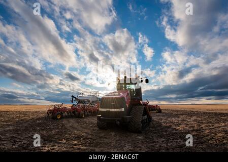 Swift Current, SK/Canada- May 9, 2020: Vast sunset sky over Case tractor and Bourgault air drill seeding equipment in Saskatchewan, Canada Stock Photo