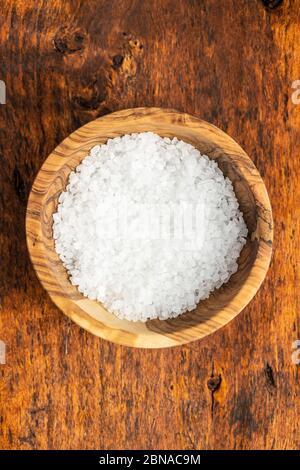 White coarse grained salt in bowl on wooden table. Top view. Stock Photo