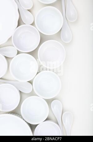 Dishware concept. White empty porcelain bowls and teaspoons background. Clean, new, luxury soup pots and spoons, vertical photo. Stock Photo