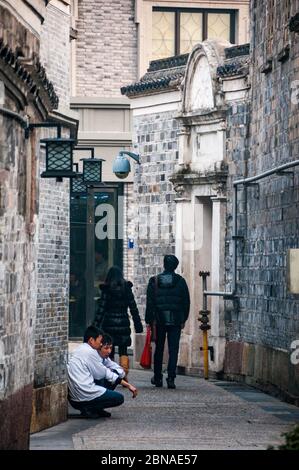 Two chefs have a break and a smoke as a couple pass by in Ningbo's Moon Lake Flourishing Garden area of restaurants and bars Stock Photo