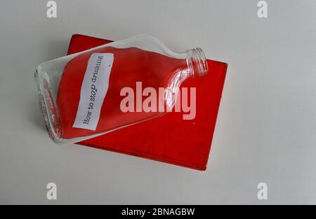 An empty glass bottle placed above old red book with title How to stop drinking, resolution concept Stock Photo