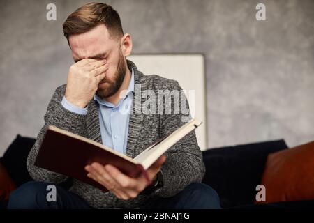 Young businessman has a headache he sitting on sofa with notepad and tired of work Stock Photo
