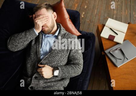 High angle view of young businessman lying on the sofa and closed his eyes with hand he tired of work Stock Photo