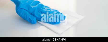 Surface cleaning against spreading of coronavirus person wearing gloves with antibacterial disinfecting wipe wiping glass table. banner panoramic background. Stock Photo