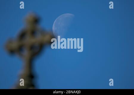 WIMBLEDON LONDON, 14 May 2020. UK. A Church cross in front of a waxing gibbous moon at sunrise over Wimbledon SW London. Credit: amer ghazzal/Alamy Live News Stock Photo