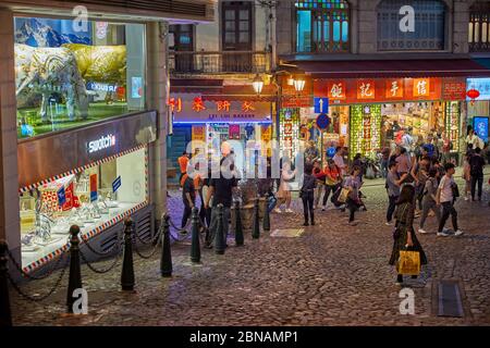 People walking on Rua de S. Paulo (Dasanba) street illuminated at night. Macau, China. Stock Photo
