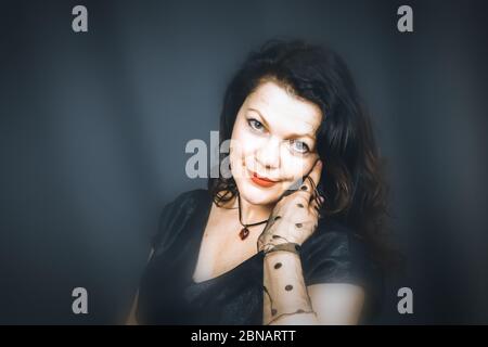 Portrait of a beautiful fashionable middle-aged woman in a black dress, posing on a dark gray background. Vintage style. The concept of preserving you Stock Photo