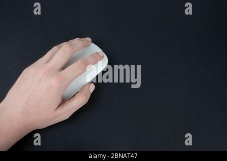 Caucasian left-handed woman using computer mouse. Female hand holding computer mouse on dark black backround. Stock Photo