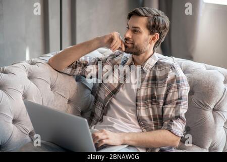 Young adult man meditating on a sofa with a laptop. Stock Photo