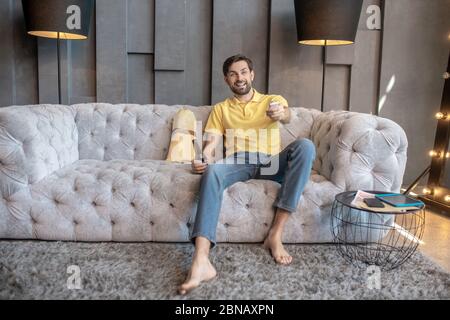 Young adult man sitting on sofa with television remote control Stock Photo
