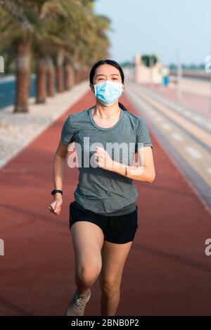 Asian woman jogging on the running track wearing protective surgical mask to prevent coronavirus spreading and stay safe