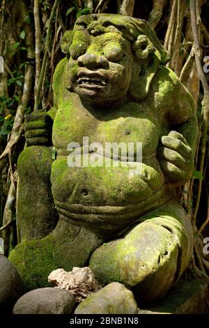 Frontal close-up view of a mossy stone statue in the Sacred Monkey Forest Sanctuary of Padangtegal, Ubud, Bali, Indonesia Stock Photo