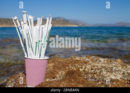 Paper drinking straws in paper cup outside on rocks next to sea Stock Photo