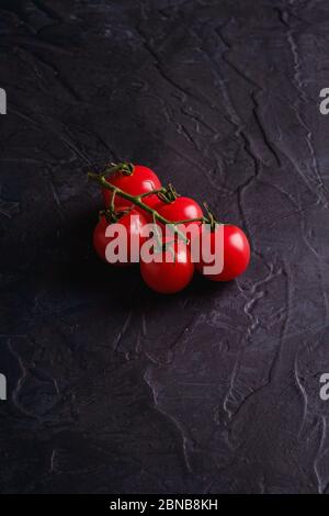 Cherry tomato branch, fresh ripe organic vegetables on dark black textured background, angle view Stock Photo