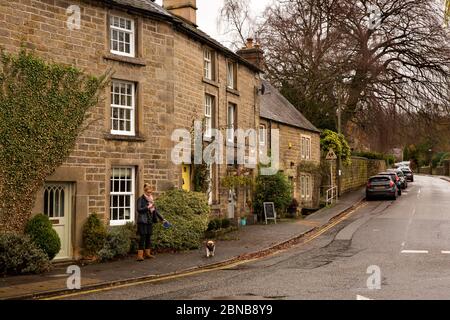 UK, England, Derbyshire, Baslow, woman dog walker at School Lane Junction below three storey stone house in winter Stock Photo